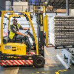 A warehouse worker maneuvers a forklift to transport crates for brewing company storage.